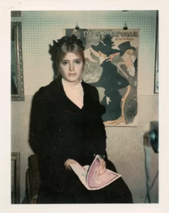 1870-1970 reference Polaroid of a young woman seated in front of a poster