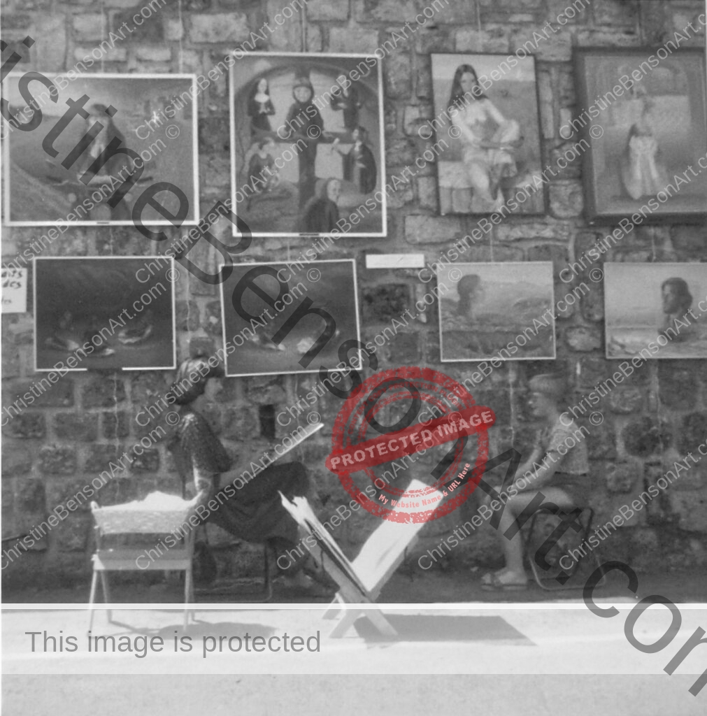 The artist sketching a boy outdoors in front of a large wall on which many of her paintings are hanging.